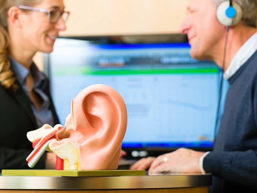 Schedule a hearing test at Amplify Hearing - this image shows a hearing test in progress with an anatomical model of an ear in the foreground