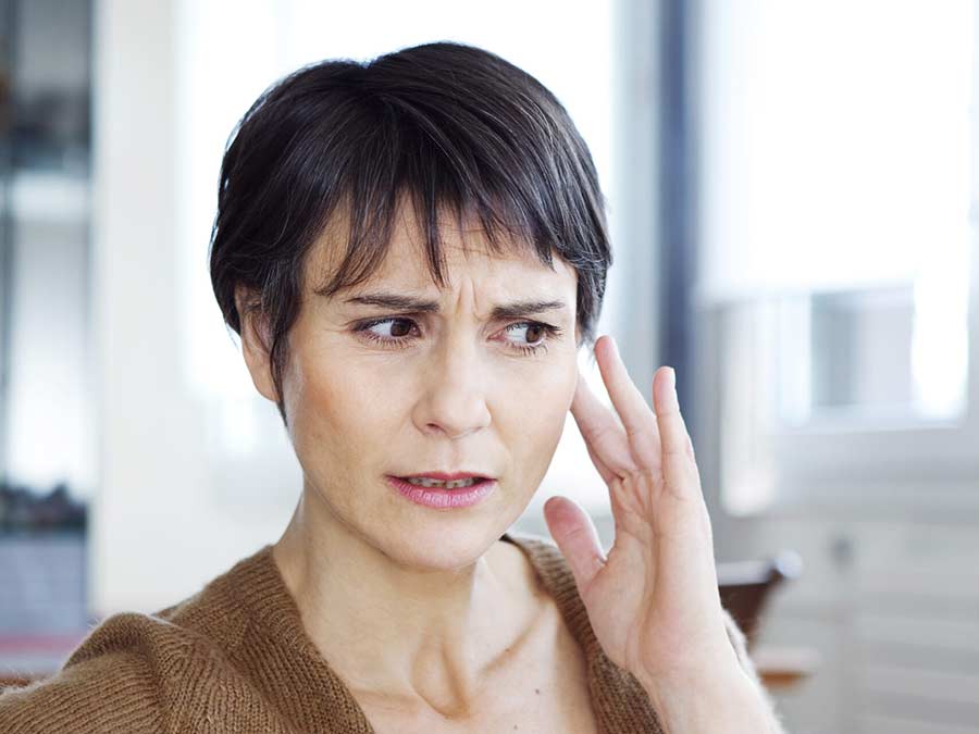 A woman suffering with hearing loss holds her hand to her left ear